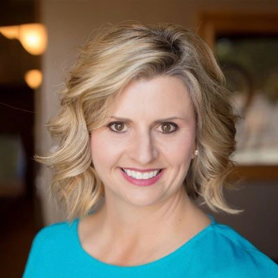 Person with short, wavy blonde hair wearing a bright teal top