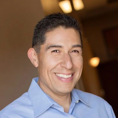Dr. Anthony Becerra wearing a light blue collared shirt standing indoors